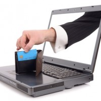 Theft over the internet concept with a hand poping out of the screen to steal a credit card, isolated on a white background